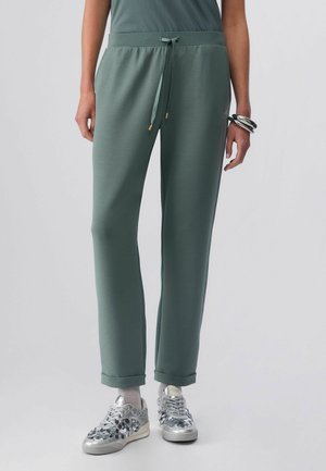 Pantaloni jogger verdi con vita regolabile con coulisse, texture sottile, gambe affusolate e risvolti arrotolati, abbinati a sneaker stampate metallizzate.