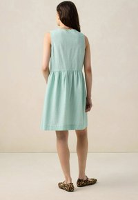 Robe sans manches de couleur vert clair, en tissu texturé, avec une taille cintrée et une jupe évasée, associée à des ballerines en imprimé léopard.