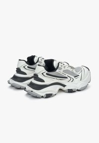 Witte en zwarte sportschoenen met een bovenwerk van mesh, een gevoerde kraag en een stevige rubberen zool met textuurdetails en gebogen accenten.