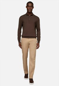 Camisa polo marrón de manga larga con cuello, combinada con pantalones chinos beige y zapatillas oscuras marrón. Tejido suave, ajuste entallado y detalles mínimos.