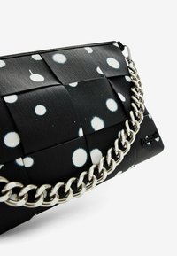 Borsa a tracolla nera con pois bianchi, tessuto testurizzato, con una catena argentata e chiusura con zip. Logo del brand impresso sul lato.
