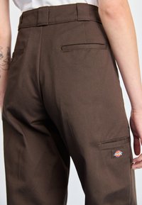 Calças cargo castanhas feitas de tecido resistente, com uma cintura alta, bolsos traseiros e um logótipo de marca distinto na bolsa lateral.
