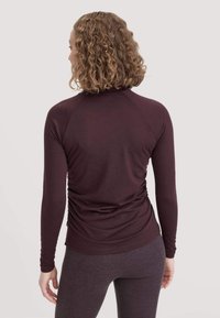 Burgunderfarbenes Langarmoberteil mit figurbetonter Silhouette, Raglanärmeln und gerafftem Rückendetail, aus weichem, strukturiertem Stoff.