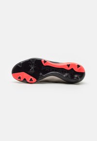 Suola delle scarpe da calcio Adidas Predator con tacchetti neri e rossi e un motivo di grip testurizzato su uno sfondo bianco.