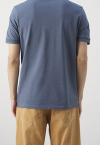 Blå bomulls t-shirt med korta ärmar, sidoflikar vid fållen, bärs med tan färgade kordbyxor. Tyget verkar slätt och lätt.