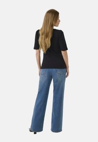 Black short-sleeve top with a fitted bodice; paired with wide-leg blue denim jeans featuring back pockets and a light wash.