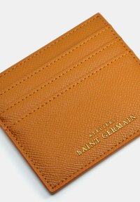 Porte-cartes en cuir orange-brun avec surface texturée, quatre fentes pour cartes et marque "Saint Germain" embossée en doré.