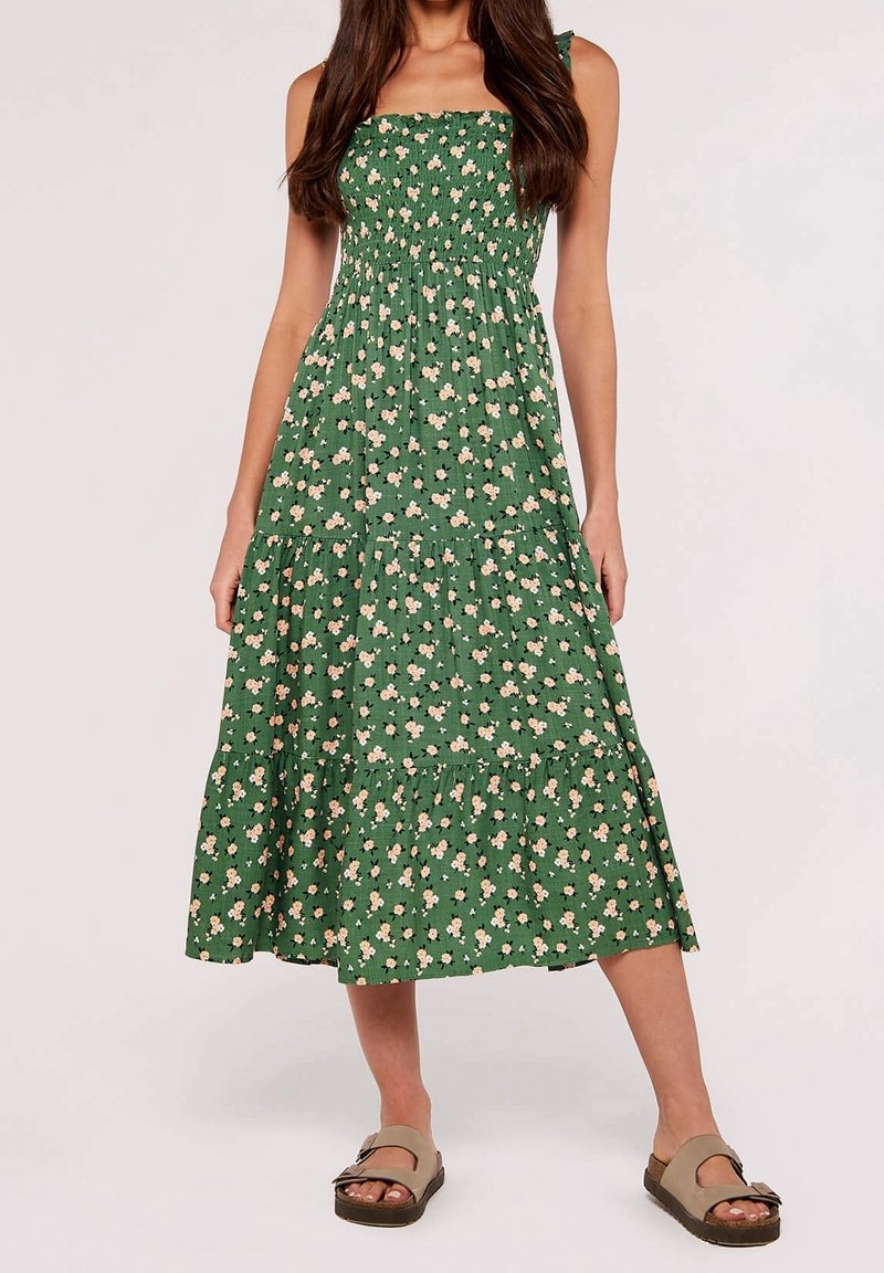 Robe florale verte avec corsage froncé, bretelles spaghetti et jupe à volants. Tissu doux avec petits motifs de fleurs roses répartis sur l'ensemble.