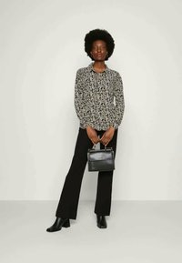 Blusa floral em preto e branco com mangas longas, frente botão, combinada com calças pretas boca de sino e uma pequena mala preta. Textura suave.