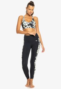 Top corto deportivo en un patrón de tie-dye en blanco y negro, combinado con leggings negros que presentan acentos laterales y una textura suave.