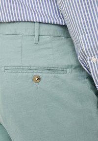 Pantaloni verde chiaro realizzati in un tessuto testurizzato, con una tasca posteriore chiusa da un bottone marrone e una vita slim.