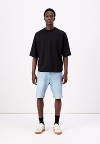 Μαύρο oversized κοντομάνικο μπλουζάκι, φωτεινές μπλε τζιν σορτς, μαύρες κάλτσες μέχρι τον αστράγαλο και λευκά αθλητικά παπούτσια με καφέ σόλες. Απλό σχέδιο, χαλαρή εφαρμογή.