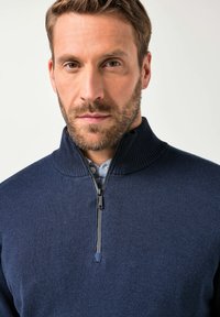 Pullover in maglina blu navy con colletto alto e mezza zip. Presenta un tessuto testurizzato e dettagli a coste nel colletto e nei polsini.