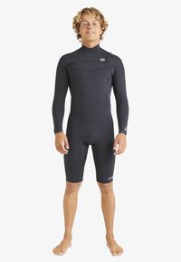 Neopreno negro con mangas largas, un escote alto y piernas cortas. Presenta un cierre delantero y una textura suave y elástica.
