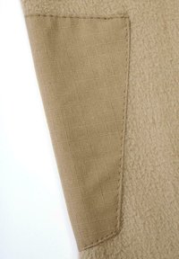 Bézs szövet, amelynek texturált, bolyhos része és sima, rácsmintás foltja van, kontrasztos varrással a szélek mentén.