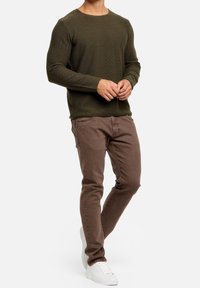 Olivgrüner Strickpulli mit strukturiertem Muster, kombiniert mit schmal geschnittenen braunen Chinos und weißen Sneakers, die ein lässiges Outfit kreieren.