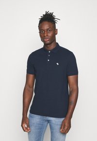 Polo shirt blu navy in cotone con colletto, patta con tre bottoni e un piccolo logo ricamato sul lato sinistro del petto.
