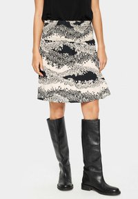 Jupe à motif floral en crème et noir, fabriquée en tissu léger avec une taille élastique, associée à des bottes en cuir noires jusqu'aux genoux.