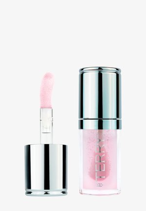 Gloss à lèvres transparent avec teinte rose clair dans un flacon transparent à bouchon argenté, applicateur partiellement retiré montrant une pointe douce et inclinée.