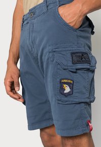 Blauwe cargoshorts van katoen met meerdere zakken, geborduurde patches op de linker dij en een rood label in de zijnnaad.