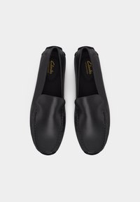 Paire de mocassins noirs en cuir avec coutures mocassin et marquage "Clarks Signature" sur la semelle intérieure, sur fond blanc.