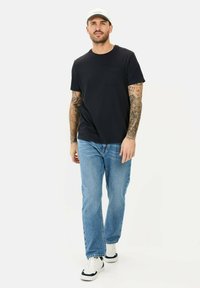 Sort kortærmet T-shirt med brystlomme, parret med lyseblå lige ben jeans og hvide sneakers, præget af et enkelt design.