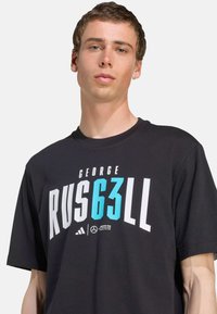Sort T-shirt lavet af bomuld, med en iøjnefaldende grafisk tekst i hvid og turkis "GEORGE RUS 63 LL" med Adidas-logoet nedenunder. Korte ærmer.