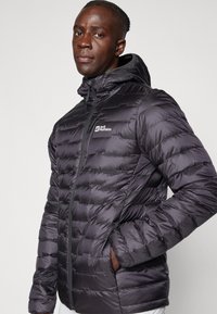 Black puffer jacket with a hood, quilted design, full zip, and side pockets. Features logo on the left chest area and a smooth texture.