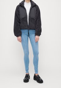 Chaqueta de forro polar gris con cremallera y acentos de tejido negro, combinada con jeans skinny azul claro y mocasines de plataforma negros.