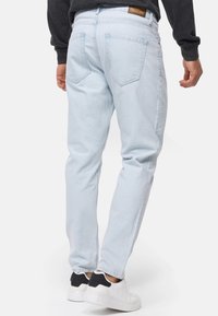 Jeans in denim azzurro chiaro con vestibilità dritta, cinque tasche e un'etichetta in pelle con il marchio sul retro. Abbinati a sneaker bianche.