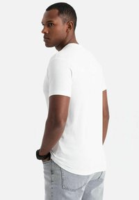 Weißes T-Shirt mit kurzen Ärmeln aus Baumwolle, mit rundem Halsausschnitt und leicht geschwungenem Saum. Getragen mit hellgrauen Jeans und einer Uhr.