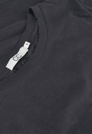 Must musta T-särk, ümmarguse kaelusega ja lühikeste varrukatega. Kaeluses on nähtav silt suurusega "S".