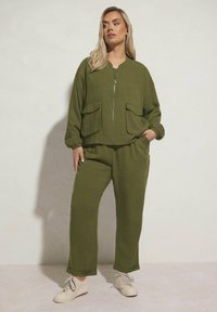 Olivgrön tvådelad outfit gjord av texturerat tyg. Jackan har dragkedja fram och två påsydda fickor, tillsammans med byxor i avslappnad passform.