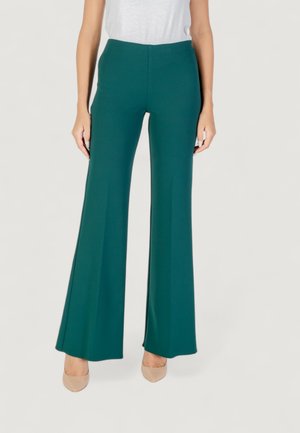 Pantaloni svasati di colore teal realizzati in un tessuto liscio e elasticizzato, con una vita alta e una silhouette pulita, abbinati a scarpe color nude.