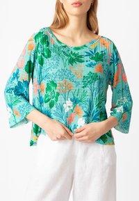 Top a fantasia floreale in turchese, con maniche a campana corte, un ampio scollo e un tessuto leggero con accenti verdi e arancioni.