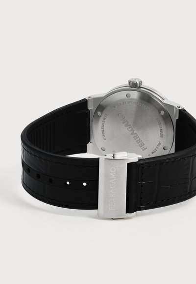 Vue arrière d'une montre-bracelet Ferragamo avec boîtier en acier inoxydable, bracelet en cuir noir et fermoir métallique gravé Ferragamo.