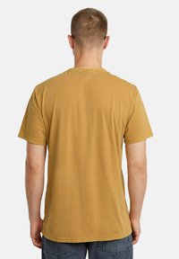 T-shirt giallo senape, maniche corte, scollatura rotonda, tessuto di cotone, texture liscia, design semplice, senza embellishments visibili.