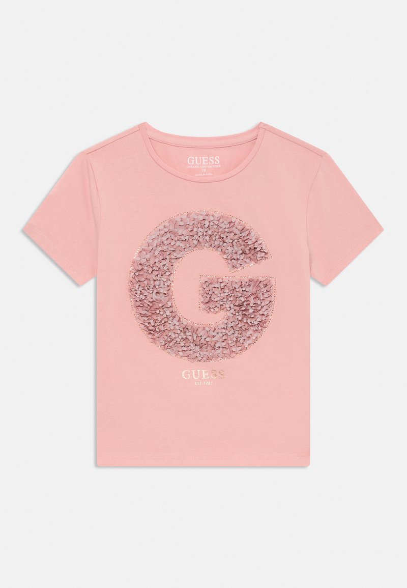 Rozā īsām piedurknēm T-krekls, kas izgatavots no organiskās kokvilnas. Uz tā ir liela, teksturēta burta "G" aplikācija ar pērļotām sekvencēm un zem tās izvietota zelta toni zīmola nosaukums.