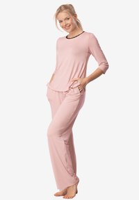 Jasnoróżowy dwuczęściowy zestaw piżamowy zawierający bluzkę z długim rękawem z czarnym koronkowym dekoltem oraz luźne spodnie z kieszeniami po bokach.