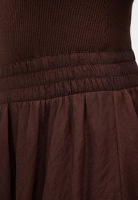 Κοντινή λήψη καφέ, ριμπ πλεκτού τοπ που είναι μαζεμένο σε μια φούστα με ραβδώσεις και υφή, με ελαστική μέση.