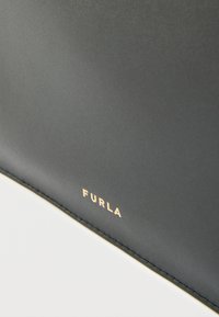 Mustast nahast ese, millel on siledapinnaline tekstuur ning kuldne "Furla" logo. Valge ääris rõhutab kontrasti tumeda materjali vastu.