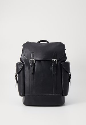 Mochila preta de couro com tampa dobrável, alças ajustáveis, ferragens prateadas, dois bolsos laterais e detalhes em costura.