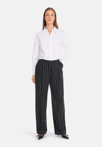 White button-up shirt paired with black pinstriped wide-leg trousers. Trousers feature side pockets and a relaxed fit. Black pointed-toe shoes.