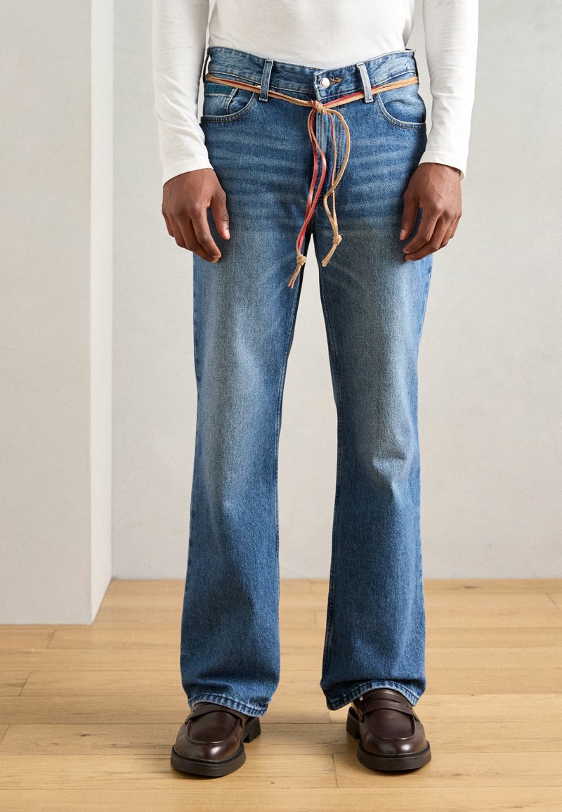 Hellblaue Denim-Jeans mit geradem Schnitt, ausgestattet mit einem gewebten, mehrfarbigen Kordelzuggürtel und einem Fünf-Taschen-Design. Strukturiertes Material, minimaler Verblassungsgrad.