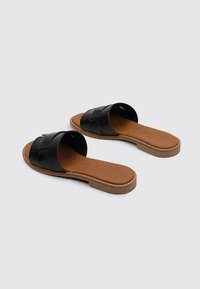 Sandales noires à lanières tressées, semelle intérieure en simili cuir marron, semelle plate et couture détaillée le long des bords.