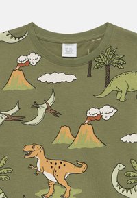 Maglietta di cotone verde con stampa di un dinosauro e un vulcano. Il design include vari dinosauri, montagne, nuvole e palme.