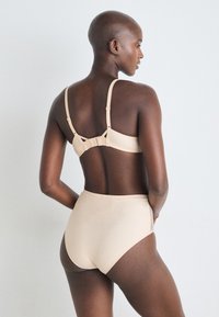 Beige bra and high-waisted briefs, made of smooth fabric, featuring adjustable straps and a hook closure at the back.
