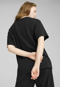 Sort bomulds t-shirt med korte ærmer, afslappet pasform, rund halsudskæring og glat tekstur. Stylet med hænderne placeret bag ryggen.