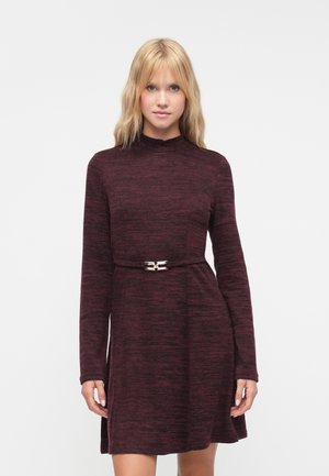 Langärmdige wijnrode jurk met een gestructureerd patroon, hoge hals en een metallic riemaccent op de taille, die zachtjes uitloopt aan de onderkant.