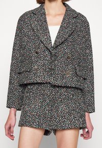 Tweed blazer with a cropped cut, featuring a mix of colors including black, green, and orange, and double-breasted button closure. Paired with matching shorts.